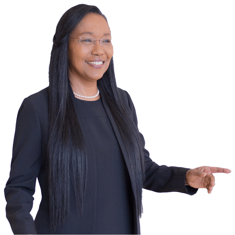 Smiling woman in a black suit and pearls gestures while speaking, conveying confidence and professionalism in a corporate setting.
