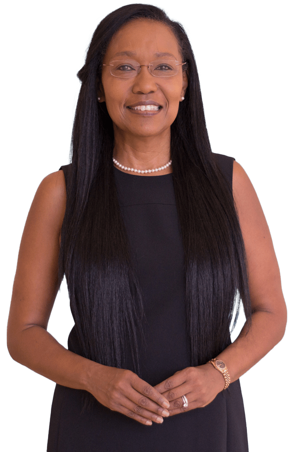 A confident woman with long hair, wearing a black dress and pearl necklace, stands against a light blue background, smiling warmly.